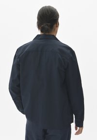 Camisa de manga larga azul marino hecha de tejido texturizado, con cuello, puños abotonados y dobladillo recto. La vista trasera resalta el diseño.