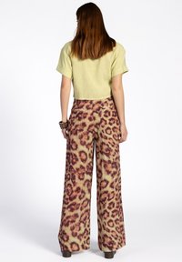 Korte lichtgroene top gecombineerd met soepel vallende broek met een bruin en oranje luipaardprint op een lichtgroene achtergrond.