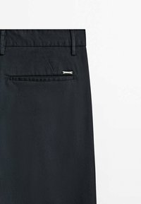 Svarta skräddarsydda byxor med en slät textur, utrustade med en bakficka med silverdetaljer och en elegant, minimalistisk design.