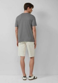 Grau kurzärmliges T-Shirt, hellbeige Shorts und weiße Sneakers mit schwarzen Akzenten. Schlichte, legere Passform ohne sichtbare Muster oder Grafiken.