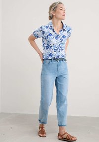 Floral short-sleeve shirt in white and blue, paired with light blue straight-leg jeans and brown strappy sandals, featuring a belt.