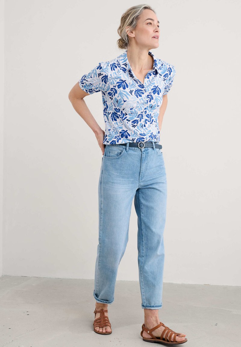 Floral short-sleeve shirt in white and blue, paired with light blue straight-leg jeans and brown strappy sandals, featuring a belt.