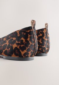 Flats à imprimé léopard en fourrure texturée avec une forme arrondie, présentant des accents noirs et un petit talon. Vue arrière mettant en valeur les détails du design.