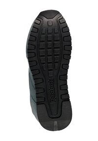 Suela exterior de goma negra con un patrón de textura en la pisada, que presenta un logo central. El material parece sintético con una parte superior de color gris.