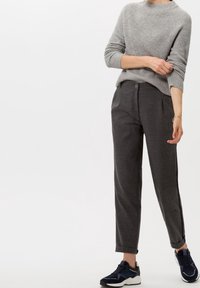 Pull gris côtelé à manches longues, associé à un pantalon ajusté gris foncé avec des plis à l'avant. Porté avec des chaussures de sport bleu marine.