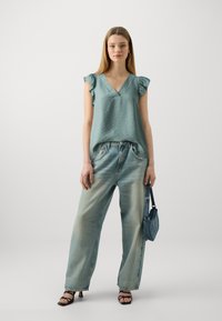 Light teal sleeveless blouse with ruffled shoulders, paired with faded wide-leg denim jeans. Accessories include a small denim handbag.