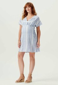 Svetlo modra in bela črtasta obleka z V-izrezom, kratkimi rokavi in A-silueto, izdelana iz mehke tkanine. Obuta v svetlo rjave sandale na klin.