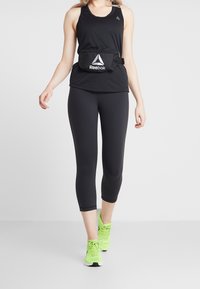 Svart sportig linne, svarta 3/4 leggings och neongröna sneakers. Inkluderar en svart Reebok midjeväska med en ficka med dragkedja och logotyp.