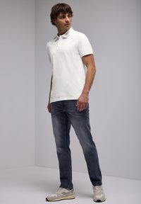 Bílá polo košile, šedé džíny a béžové tenisky. Polo má klasický límec a krátké rukávy, s hladkou texturou.