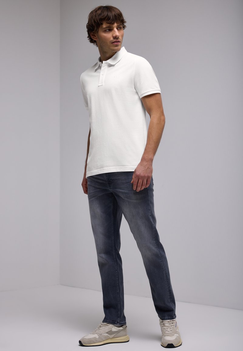 Bílá polo košile, šedé džíny a béžové tenisky. Polo má klasický límec a krátké rukávy, s hladkou texturou.