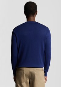 Maglione lavorato a maglia blu navy con maniche lunghe, polsini a coste e scollo rotondo, abbinato a pantaloni beige chiaro.