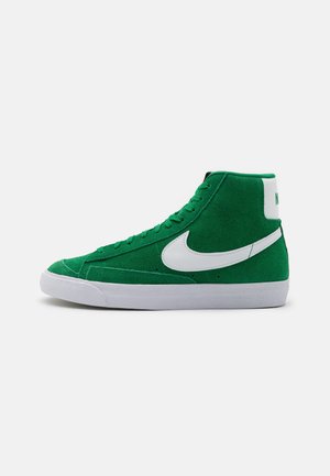 Zapatilla alta verde de ante con el logo de Nike en blanco, suela blanca y cordones en la parte delantera. Presenta una superficie texturizada y un cuello acolchado.