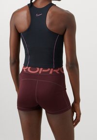 Débardeur de sport noir avec coutures roses et un petit logo, associé à un short bordeaux avec une large ceinture "PRO".