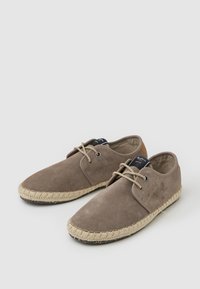 Zapatos de ante marrón con puntera redonda, cierre con cordones y suela de yute estilo alpargata. Textura suave y diseño minimalista.