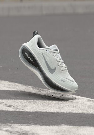 Fehér és szürke Nike ZoomX futócipő, amely lebeg egy jelzett aszfaltfelület felett, a talp körül szennyeződésrészecskékkel.