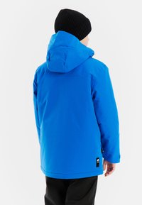 Blaue isolierte Jacke mit Kapuze, aus glattem, wasserabweisendem Material. Verfügt über ein schwarzes Etikett am unteren Ende und hat eine lässige Passform.