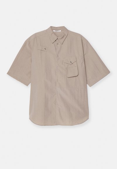 Kortärmad skjorta med knappar i ljusbeige tyg. Har en bröstficka med ficklock och tryckknappsstängning. Slät textur, rundad fåll.