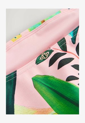 Tessuto rosa con stampa di foglie verdi e cuciture dettagliate, con un piccolo emblema logo metallico rotondo cucito vicino a una cucitura.