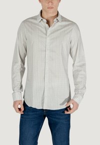 Camicia bianca a maniche lunghe con un motivo sottile, colletto button-down e design aderente, abbinata a jeans blu scuro.