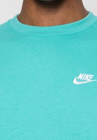 Turkos bomullströja med rundad halsringning och ribbad textur. Har en liten vit Nike-logotyp på vänster sida.