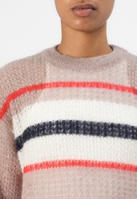 Gebreide trui in licht taupe met drie horizontale strepen: rood, wit en marineblauw. Zacht, textuurmateriaal met een ronde halslijn.