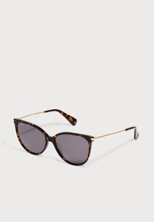 Gafas de sol de ojo de gato con montura carey, lentes oscuras y finas varillas doradas reposando sobre una superficie blanca.