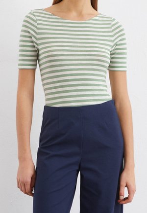 Pasiasty zielono-biały top z krótkim rękawem i dekoltem łódkowym, w połączeniu z granatowymi spodniami o wysokim stanie, podkreślającymi dopasowany krój.