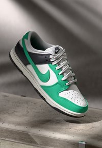 Τα sneakers Nike Dunk διαθέτουν πράσινο δερμάτινο επάνω μέρος με λευκές και γκρίζες λεπτομέρειες, παχύ κολάρο, τρυπητό μπροστινό παπούτσι και λευκά κορδόνια.