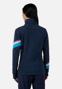 Giacca in fleece blu navy con colletto alto, caratterizzata da strisce tricolori (rosa, azzurro e bianco) sulla manica sinistra. Texture liscia.