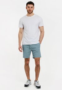 T-shirt bianca a maniche corte abbinata a pantaloni corti azzurri chiari, con cintura elastica, tasche laterali e sneakers grigie e blu.