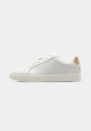 Zapatilla de cuero blanca con una textura suave, punta redondeada y cordones finos. Presenta un acento de logo dorado y un tacón beige moteado.