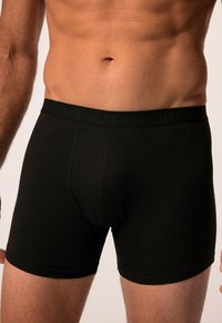 Černé boxerky vyroben�é z měkkého materiálu, s elastickým pasem s vyraženým logem a přiléhavým střihem. Bez vzorů nebo dalších akcentů.