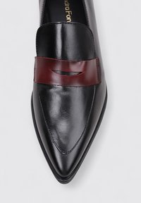 Zapato de cuero negro con punta afilada y acabado liso. Presenta una correa de cuero burdeos cruzando la parte superior con un detalle cortado. Suela plana.