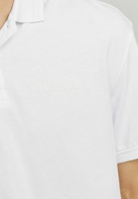 Cămașă polo albă din bumbac, cu un material texturat. Prezintă un logo subtileembossat care spune "ORIGINALS JACK&JONES" pe piept.