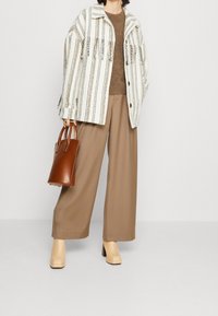 Giacca a righe sovradimensionata bianca e beige, maglione marrone, pantaloni larghi marroni, stivali con tacco blocco beige e una piccola borsa marrone.