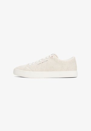 Zapatillas de lona beige con cordones blancos, punta redonda y una suela blanca gruesa. Presenta un sutil detalle del logo en el costado.