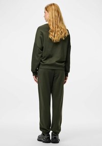 Bluza w kolorze oliwkowej zieleni i dopasowane spodnie dresowe z miękkiego materiału, o luźnym kroju i elastycznych mankietach, zestawione z czarnymi butami sportowymi.