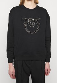 Felpa nera con grafica trapuntata e paillettes raffigurante due farfalle all'interno di un disegno circolare sul davanti. Polsini e orlo a costine.