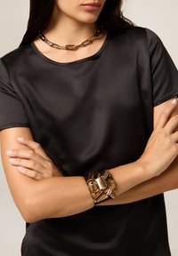 T-shirt nera in satin con maniche corte, abbinata a un bracciale in catena dorata spessa e a una collana coordinata con grandi anelli.
