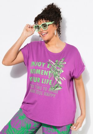 Paarse t-shirt met korte mouwen met groene grafische tekst en bladontwerp. Gecombineerd met gepersonaliseerde groene en paarse broeken. Transparante groene zonnebril.