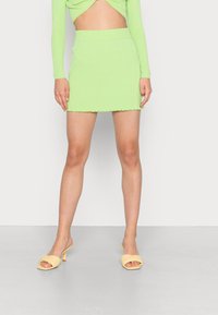 Top corto verde con canalé y corte, combinado con una minifalda verde a juego con un dobladillo con volantes. Llevado con mules amarillos de tacón.