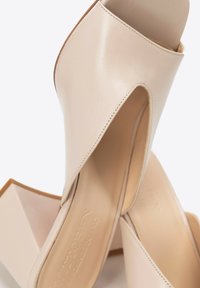 Scarpe col tacco alto in pelle beige con punta aperta e design ritagliato, caratterizzate da una texture liscia e un tacco a blocco affusolato.