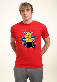 Rød bomulds T-shirt med en gul bjørn dukke, der kommer frem fra en tryllehat, med farverige stjerner og grafiske detaljer.