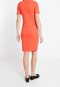 Bodycon-klänning i klar korall, korta ärmar, knälängd, tillverkad av stretchigt material, slät textur, matchad med svarta flats.