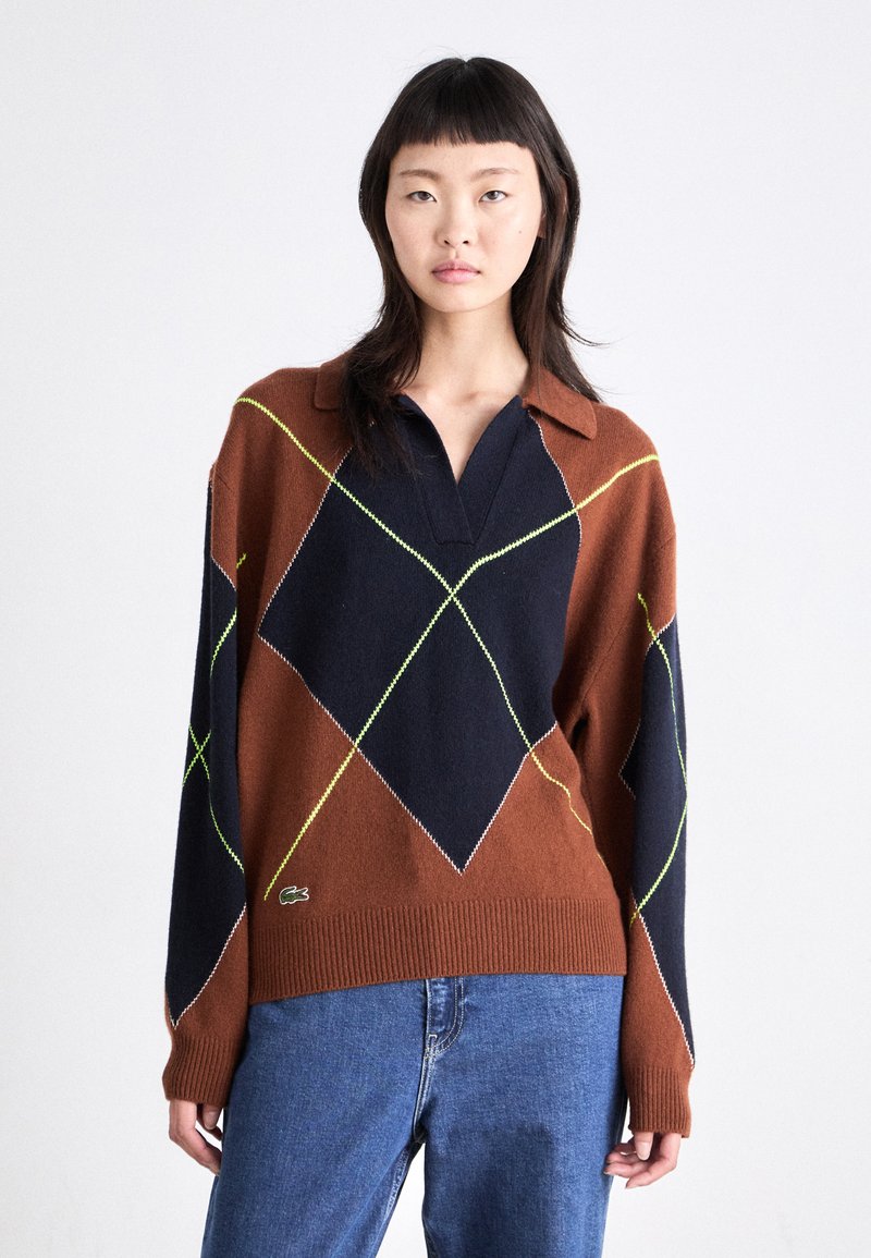 Pull en tricot argyle marron et bleu marine avec des accents vert lime, col avec boutons, et ourlet côtelé. Manches longues et logo de la marque en bas.