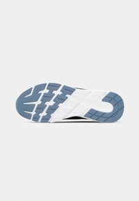 Semelle d'une basket noire et blanche avec des motifs de bande de roulement bleus au talon et à l'avant-pied, présentée sur un fond clair uni.