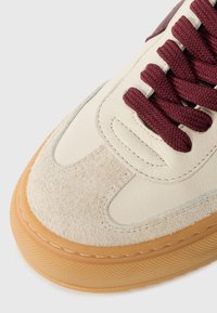 Cream leather sneaker with maroon laces, suede accents, and a textured gum rubber sole. Features stitching details and rounded toe design.