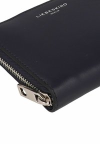 Portafoglio in pelle blu navy con cerniera in tonalità argento, caratterizzato da un design minimalista e dal nome del marchio impresso sul fronte. Texture liscia.