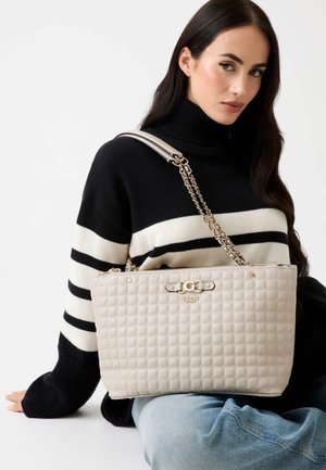 Bolso tote acolchado beige con asa de cadena y herrajes dorados. Presenta detalle de logo y cierre con cremallera, con una forma rectangular estructurada.