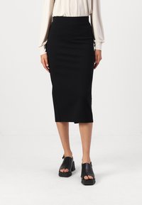 Svart midi blyantskjørt med en tettsittende design, glatt tekstur og høy midje. Fått sammen med svarte åpen tå blokkhæler.